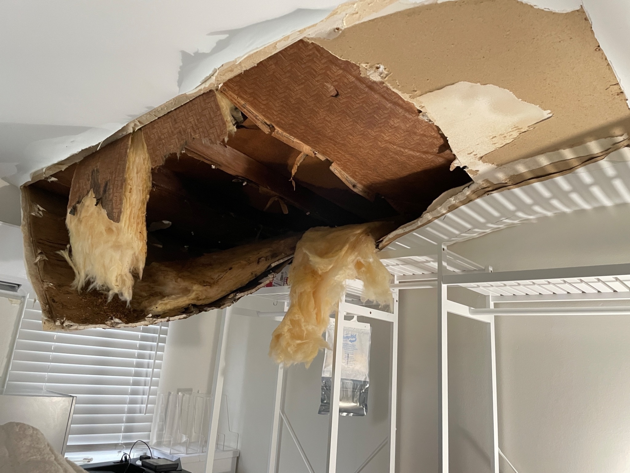 A collapsed roof and ceiling opening hangs directly over a bed covered in debris.