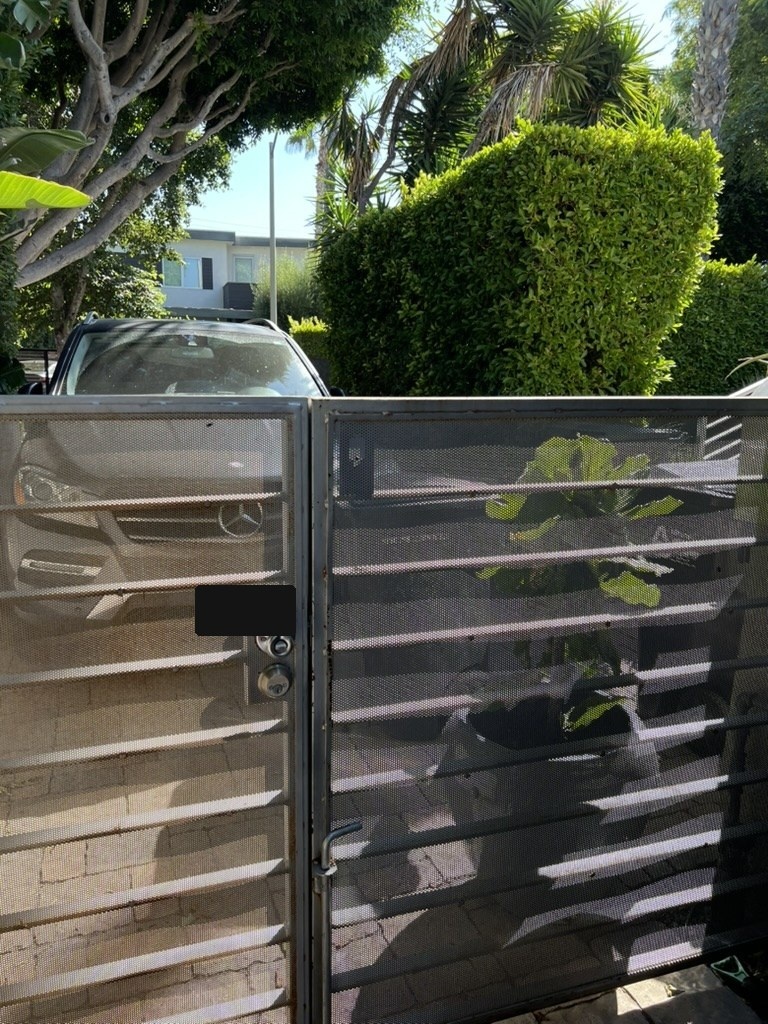 A vehicle backed immediately against the exterior side of the gate; the visible license plate is permanently obscured.