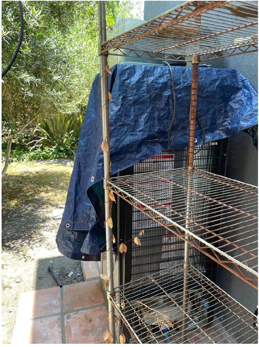 Discarded refrigerator covered by a tarp and placed directly in front of the only kitchen window